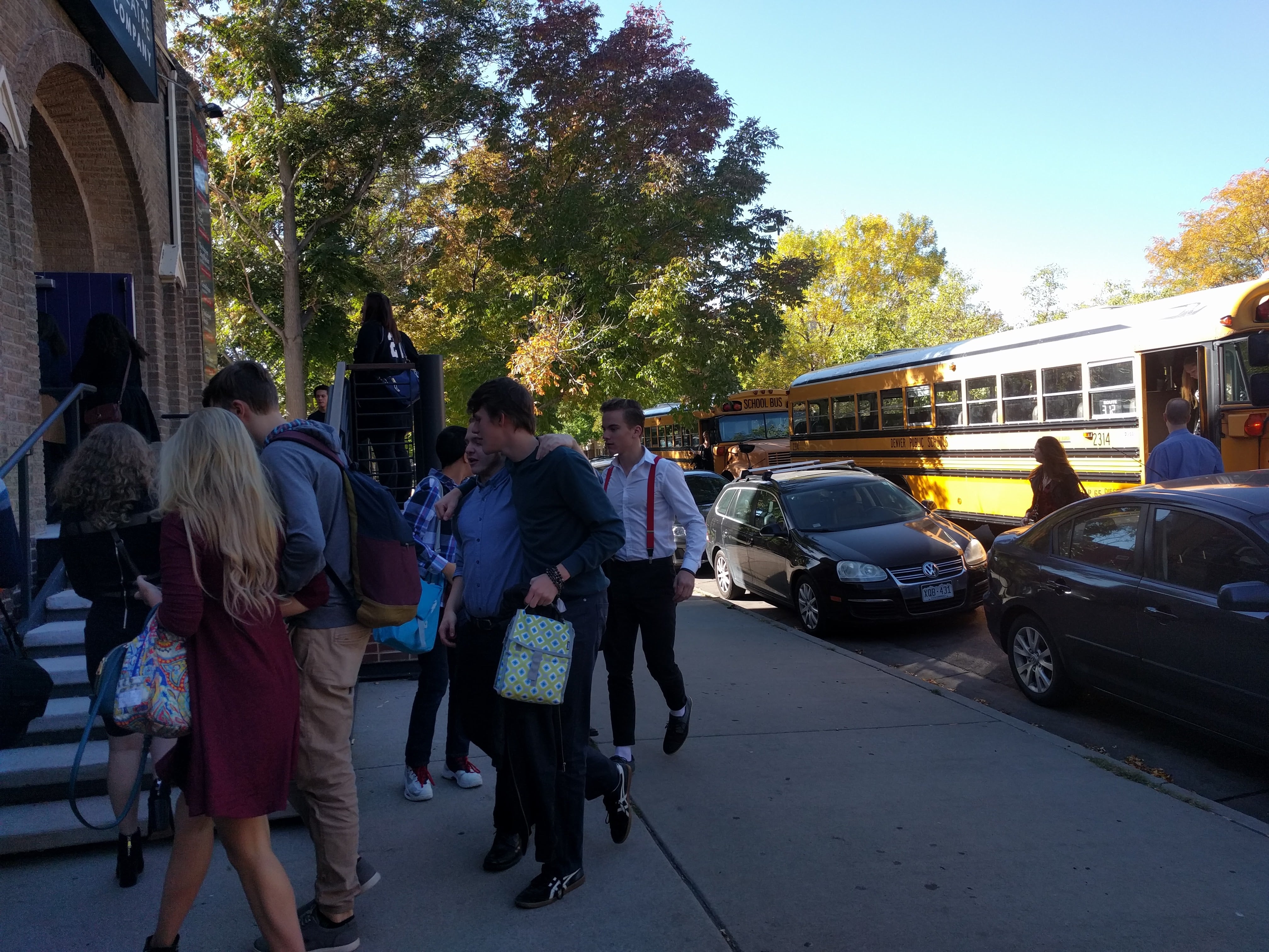 A crowd of students walk into the Curious Theatre building on a bright, sunny day.