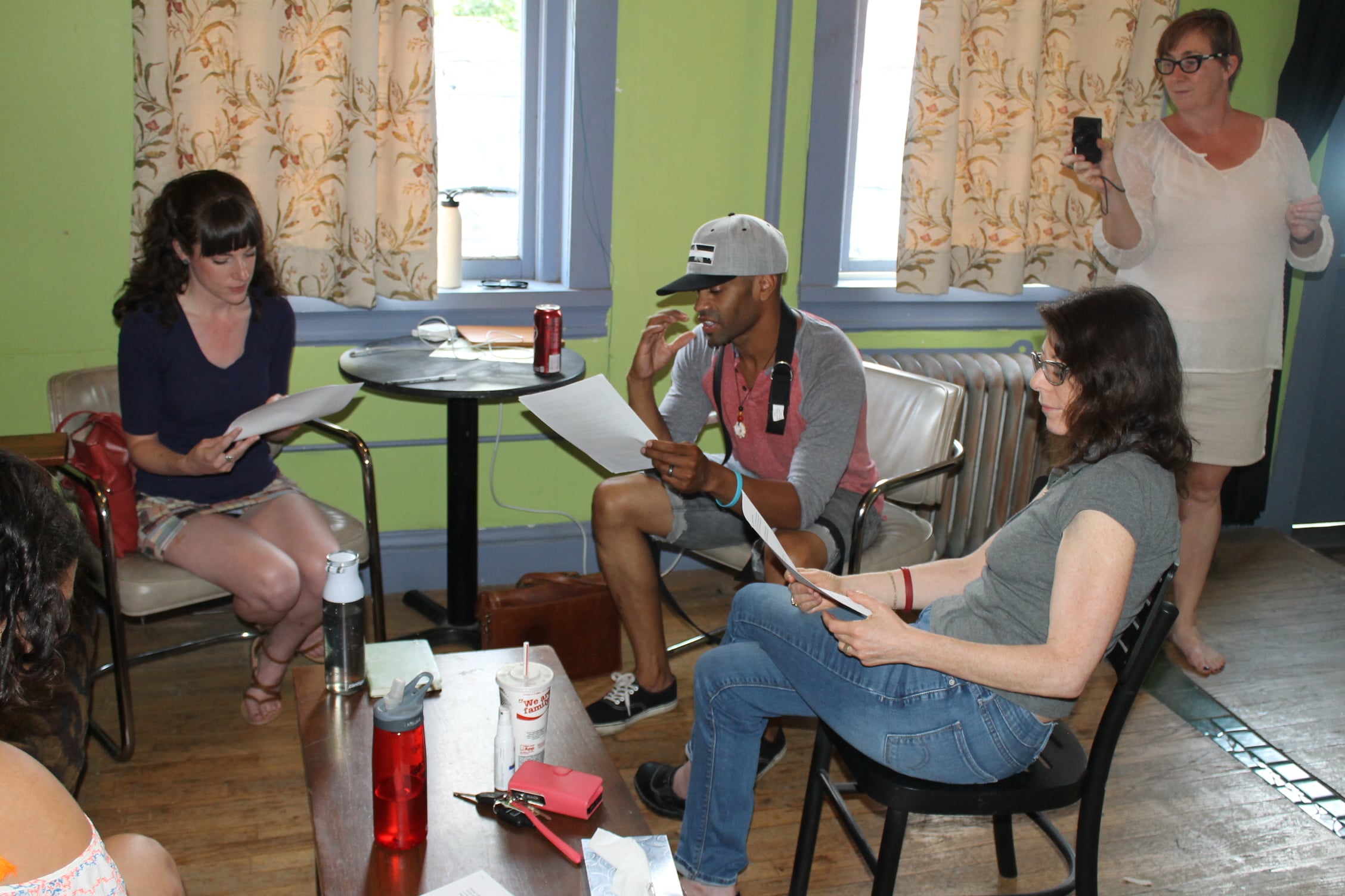 Actors sit at a kitchen table and rehearse their lines.