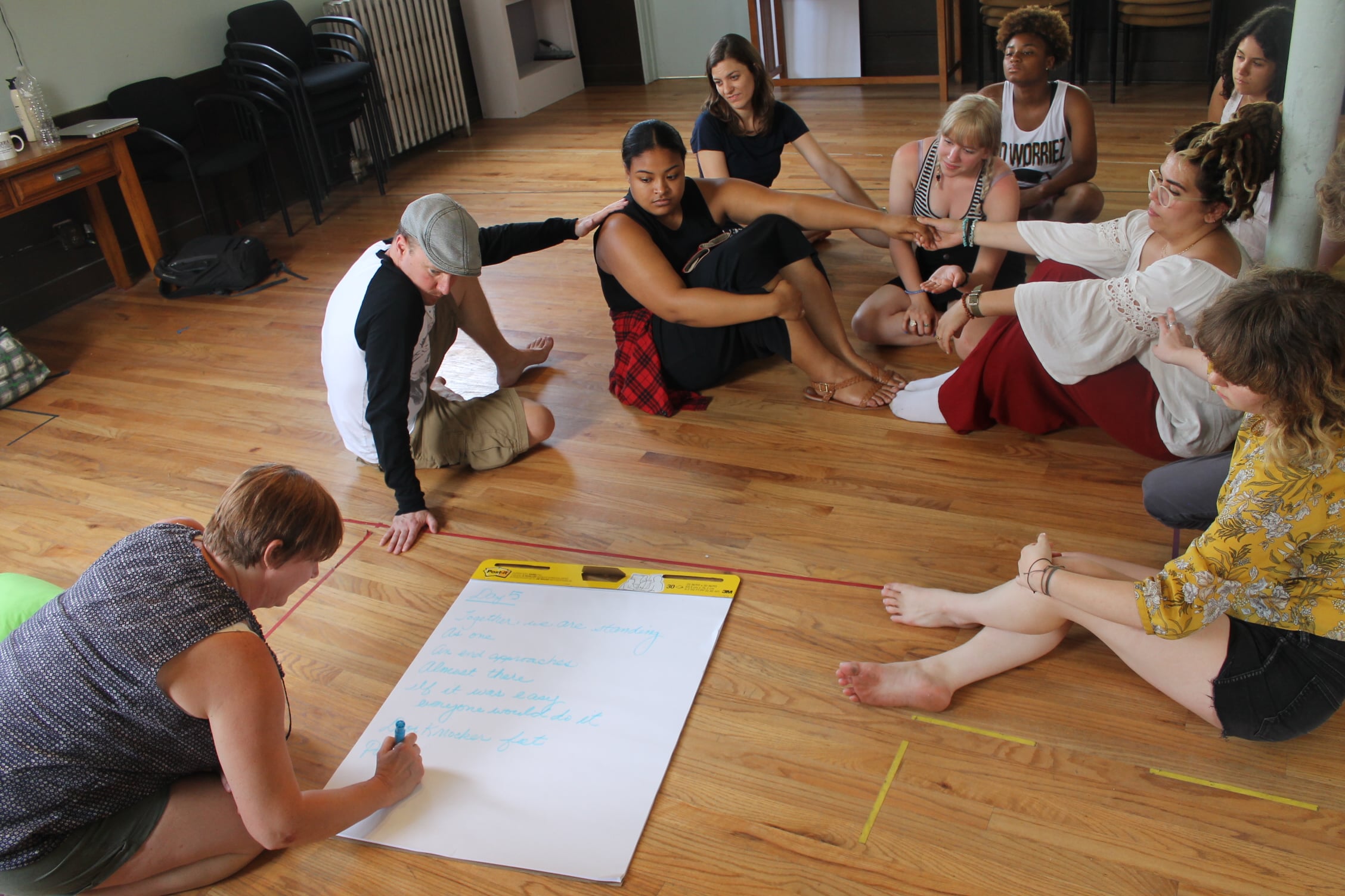 Actors sit together on the floor and participate in team-building activities.
